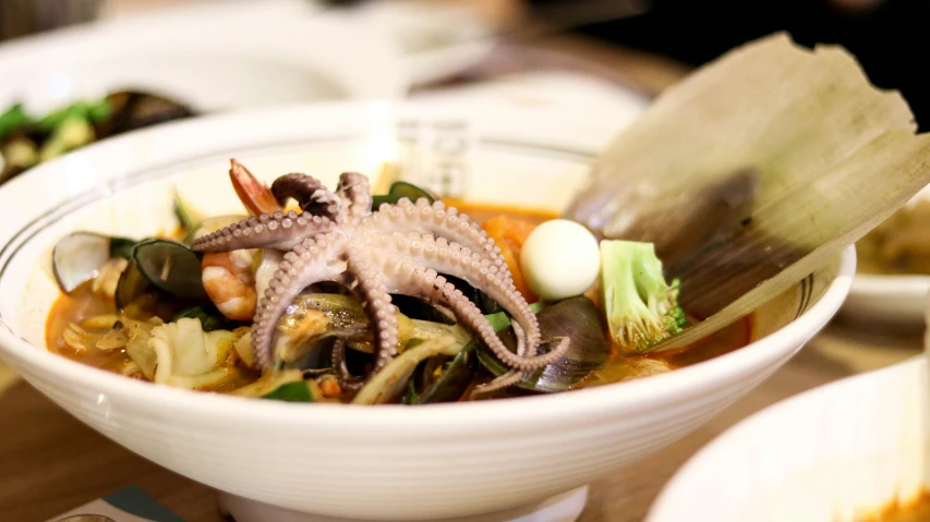 bowl of asian food with an octo, carrots and a broth