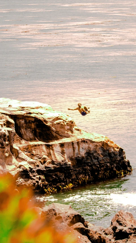 the surfer is jumping off of the rocks into the water