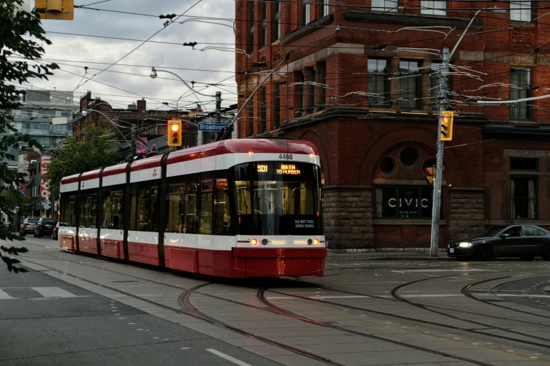 red trolley driving on street with city building on either side