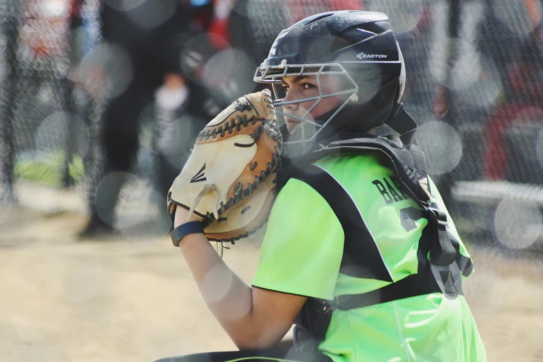 boy in helmet and green shirt sitting with his mitt