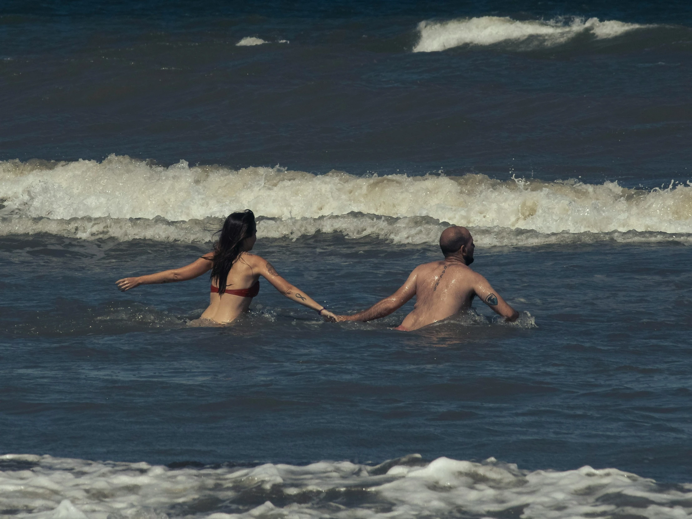 a man and woman in the ocean holding hands