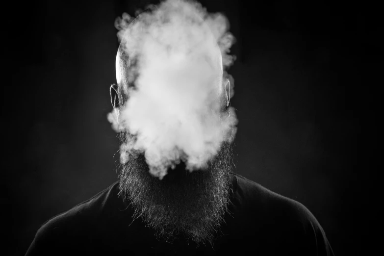 a man with a beard is in the dark while holding onto smoke