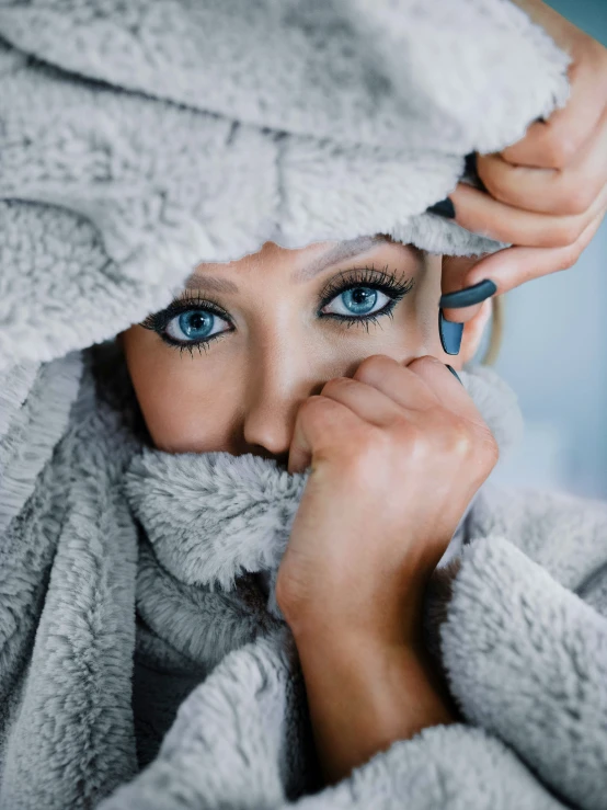 a woman in a gray coat is covering her face with a towel