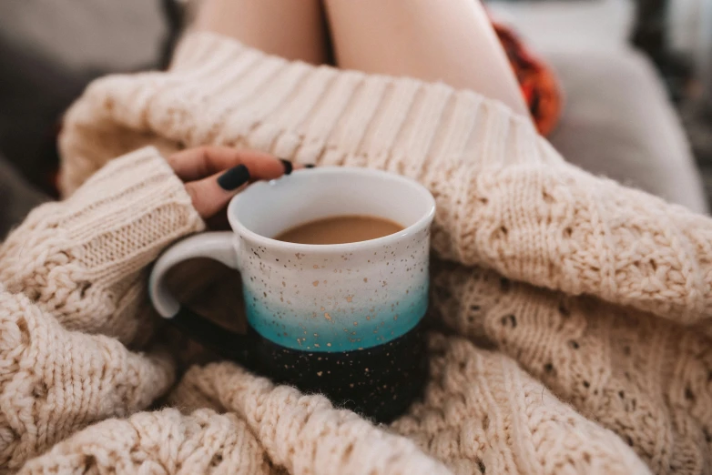 person laying on couch holding cup of coffee