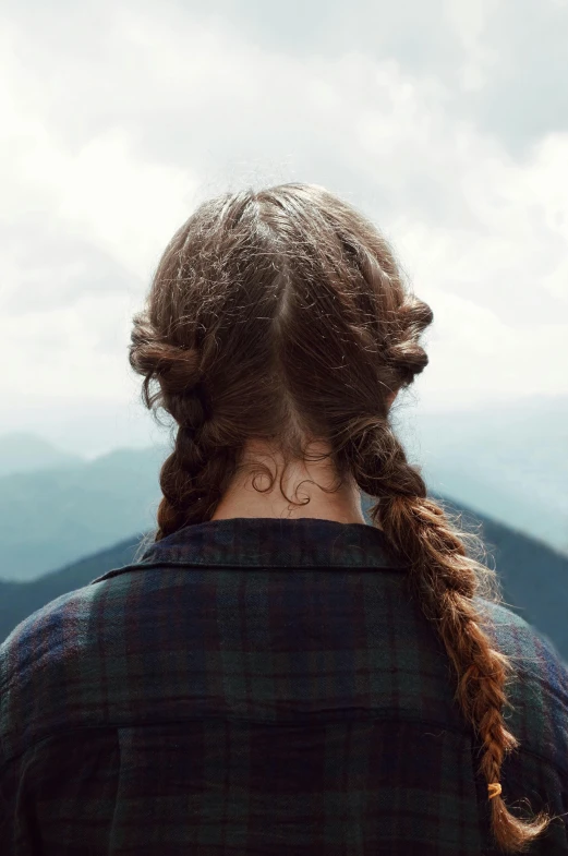 the back view of a woman with her hair in ids standing near a mountain range