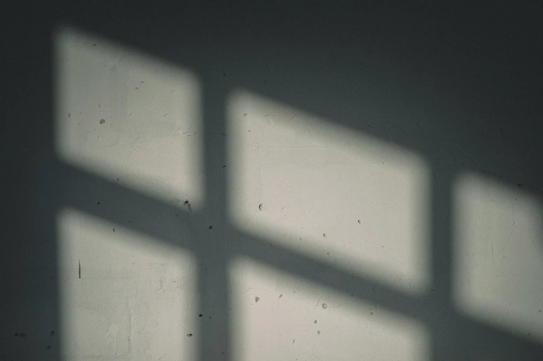 the light and shadow from a window are cast on a wall