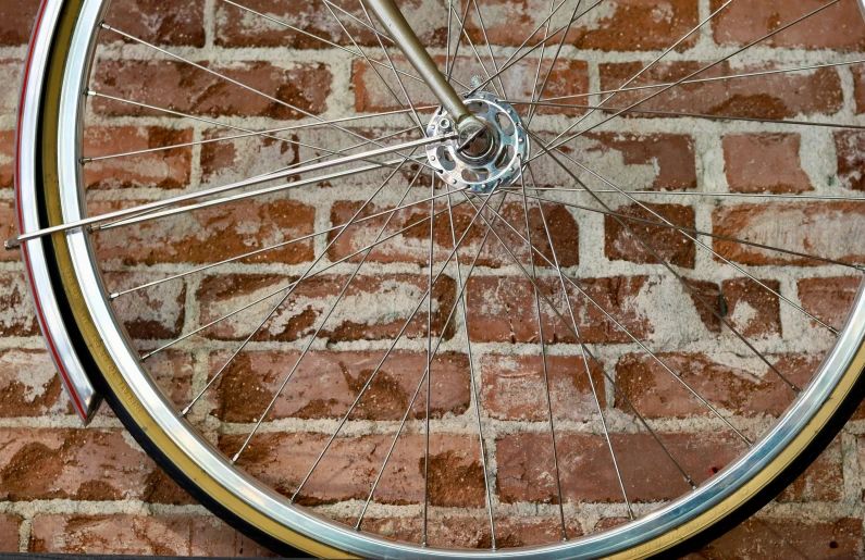 a close up of a spoke of a bicycle near a brick wall