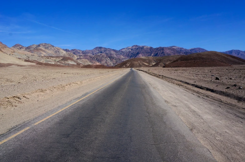 a long road stretches across mountains with rocks and desert