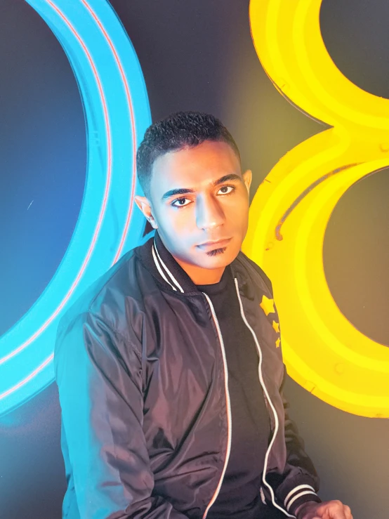 an attractive young man sitting in front of a neon blue and yellow sign