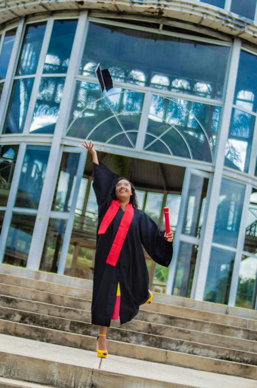 a woman in graduation attire throwing a red and black ball