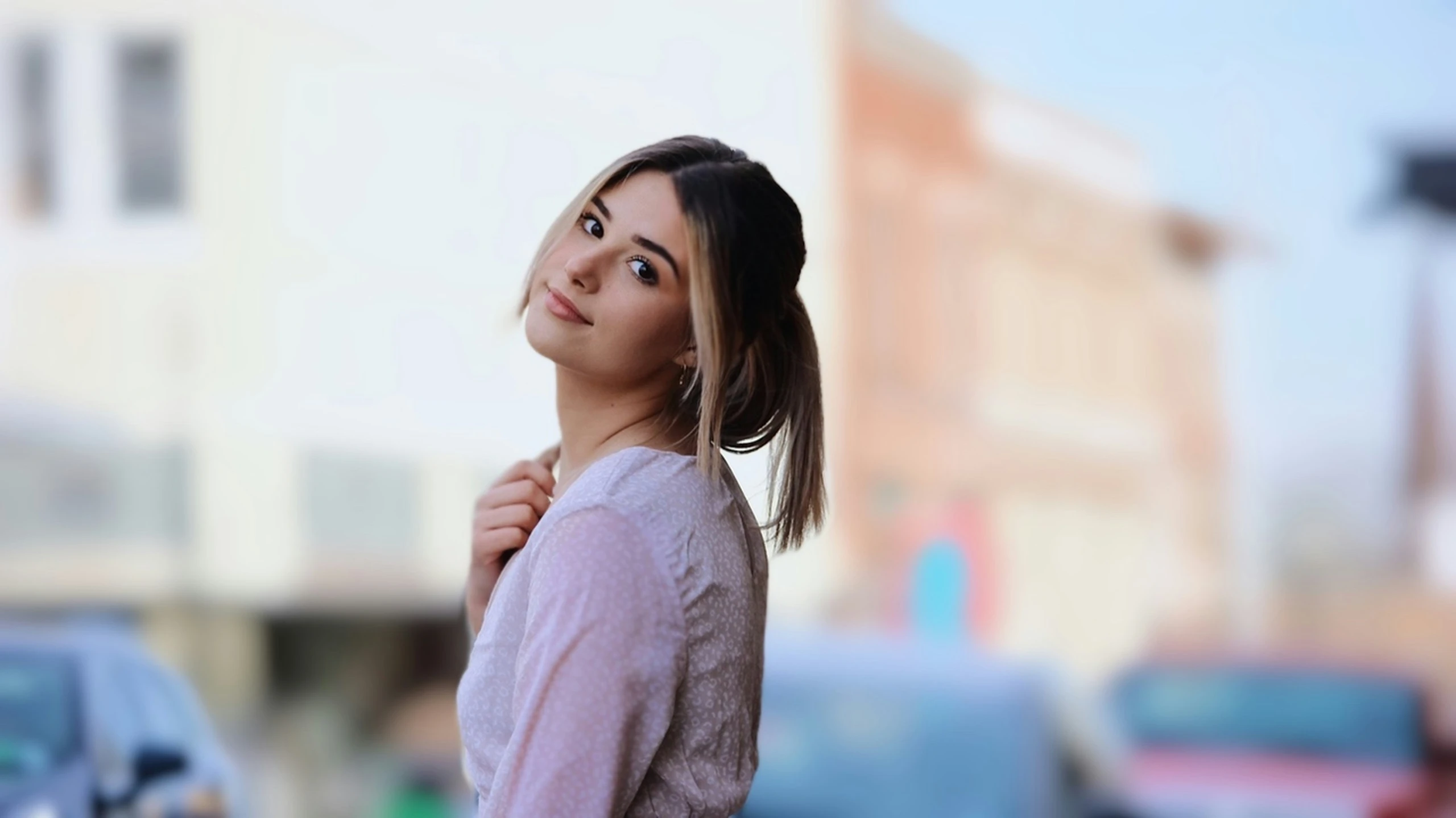 a young woman standing near a street with a car behind her