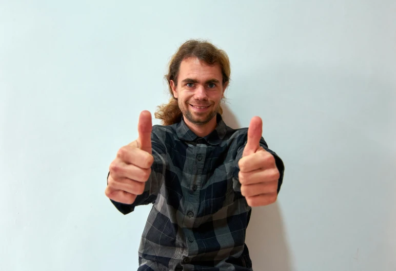 a young man giving two thumbs up in front of a blue wall