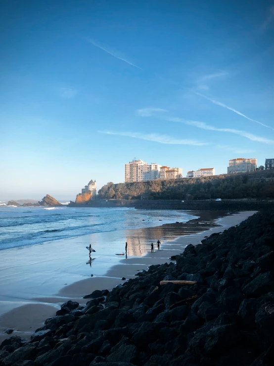 three people are walking along the shore while buildings are in the distance