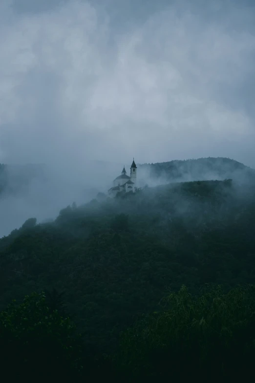 fog is covering a hill in front of a steeple