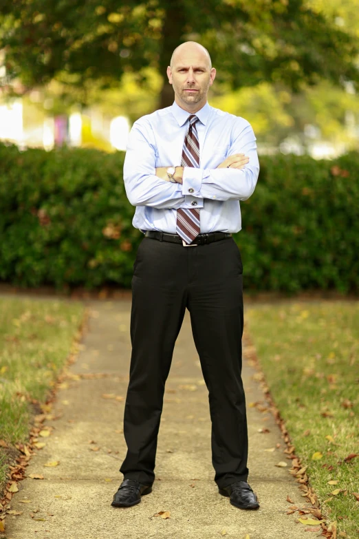 a man in a blue shirt and tie standing in front of a tree