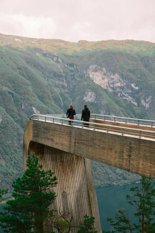 two people on top of a tall bridge in the mountains