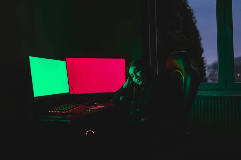 the dark room has two neon colored monitors