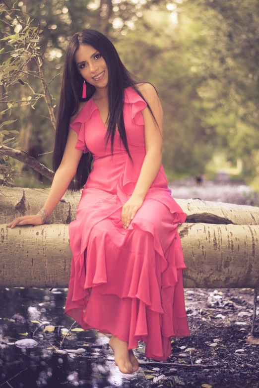 a beautiful young lady wearing a pink dress on a tree nch