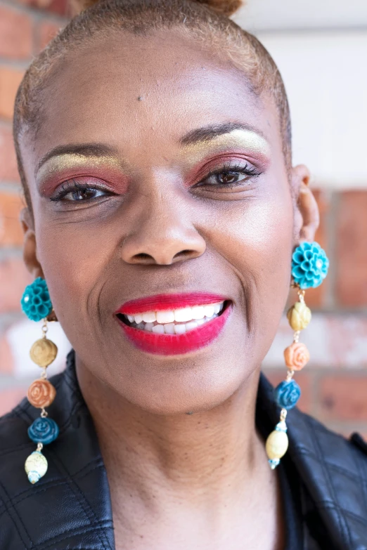 a woman with earrings on smiling in front of a brick wall