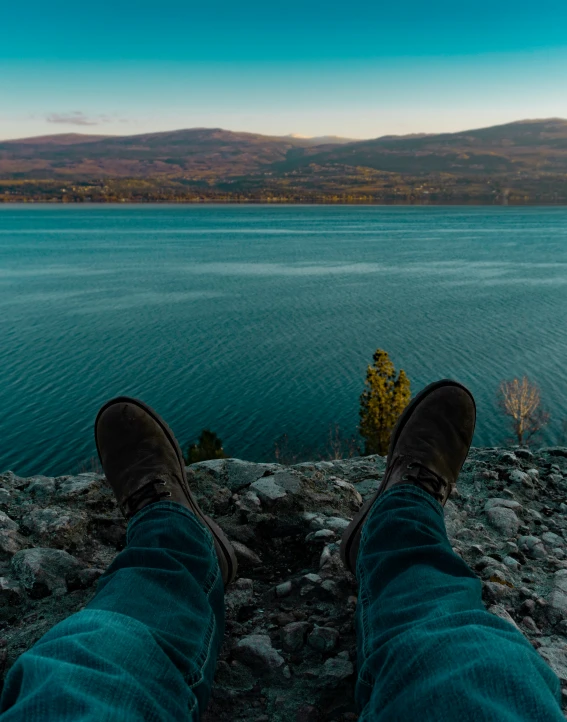 person's feet on the rocks with a body of water in the background