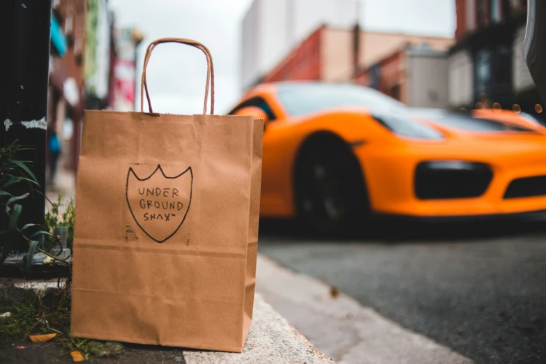 brown bag on the street in front of a bright orange sports car