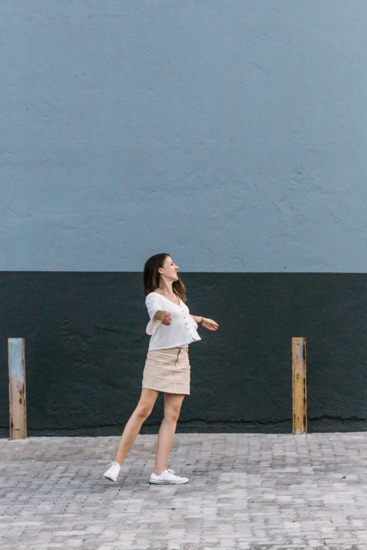 a young woman in a white top and tan skirt throwing a frisbee