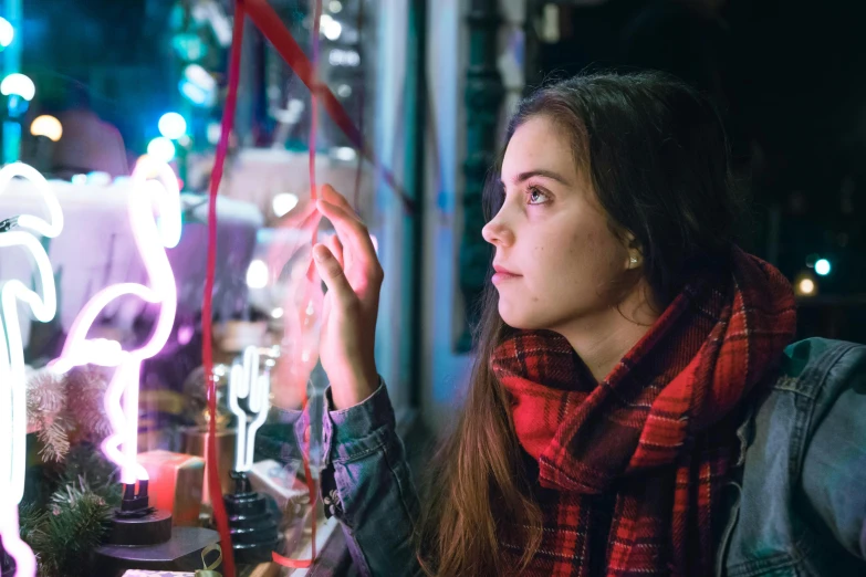 a woman wearing a scarf looks at neon lights