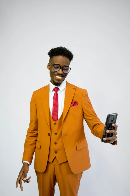 a man wearing orange suit and red tie holding up a cellphone