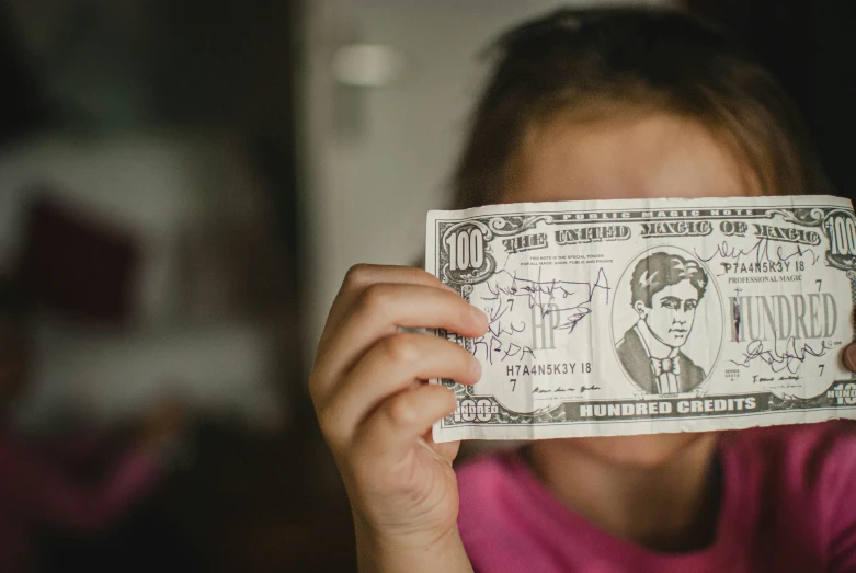 a little girl holding up a $ 50 bill