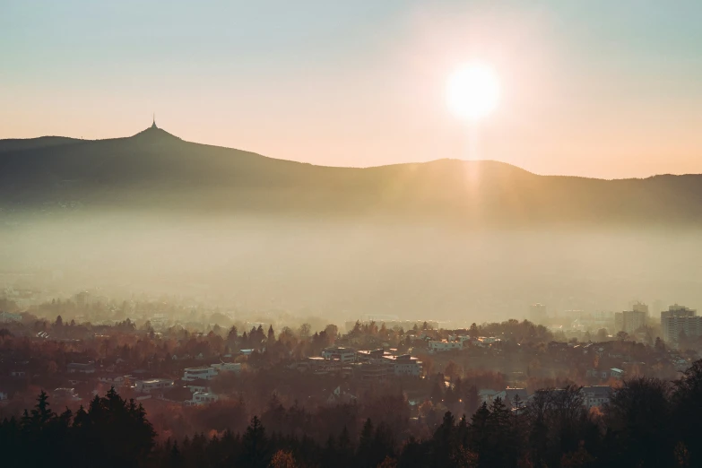 the sun peeks through the fog that sits on a hill above a small town