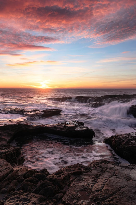 the sun is setting over the ocean with waves crashing in