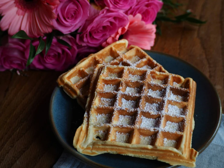 two waffles are sitting on a plate near a bouquet of flowers