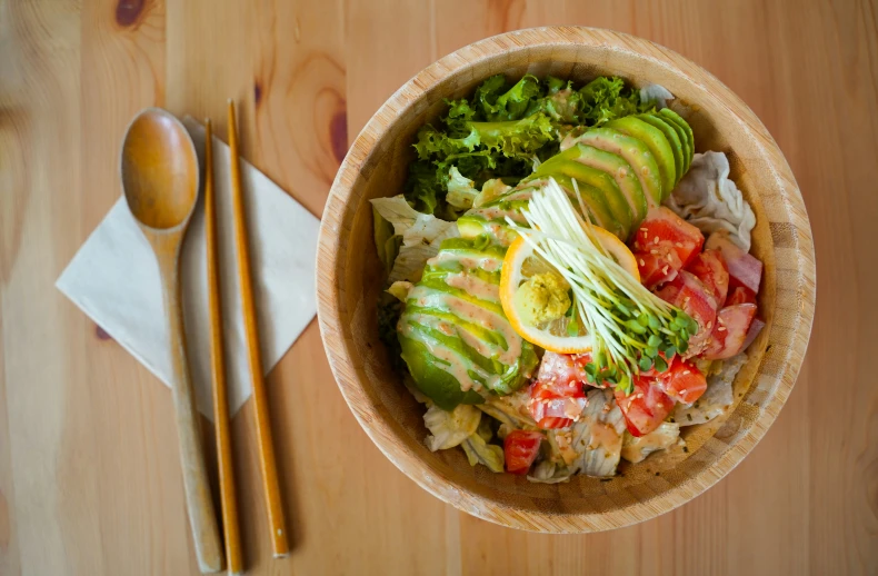 a wooden bowl filled with greens and tomatoes