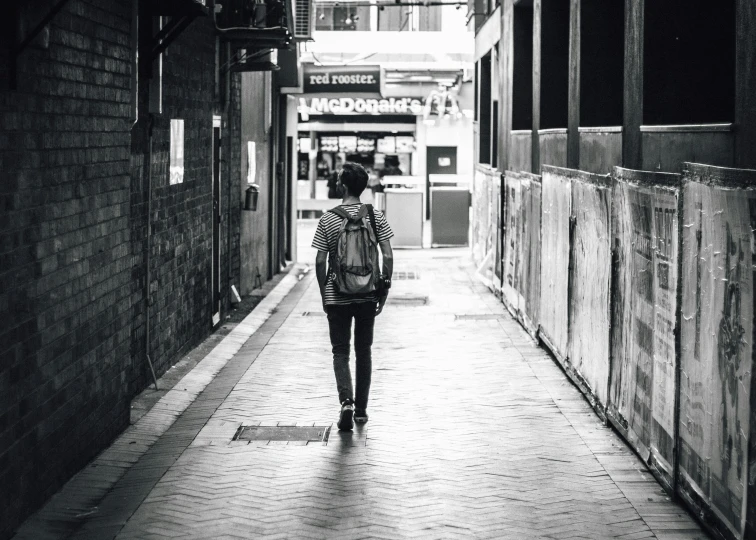 woman with back pack walking on city street near stores