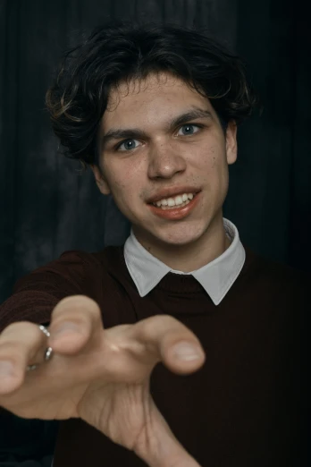 a young man in a brown sweater making a hand gesture