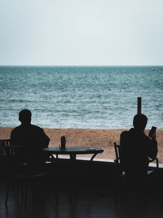 two men sitting at an outside table looking out over the water