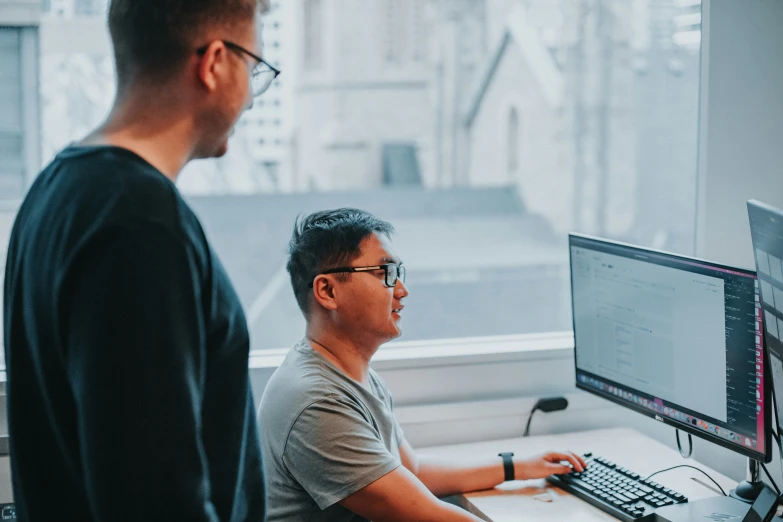 two men standing in front of a computer in a room