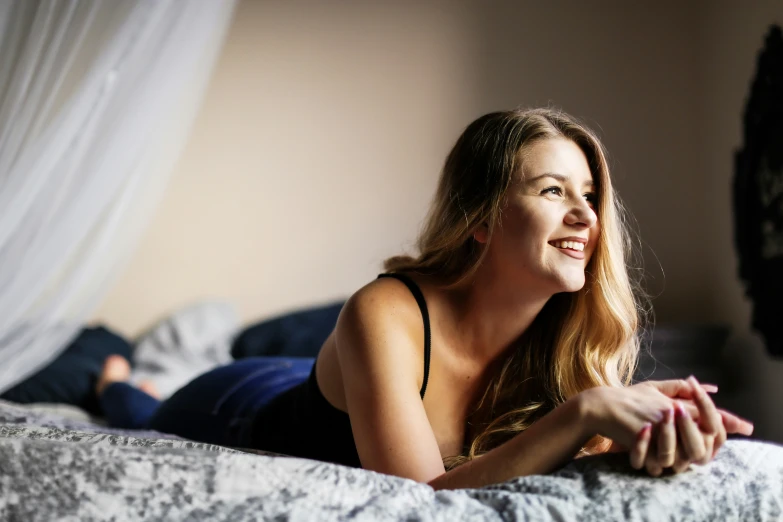 young woman in black top laying on the edge of a bed