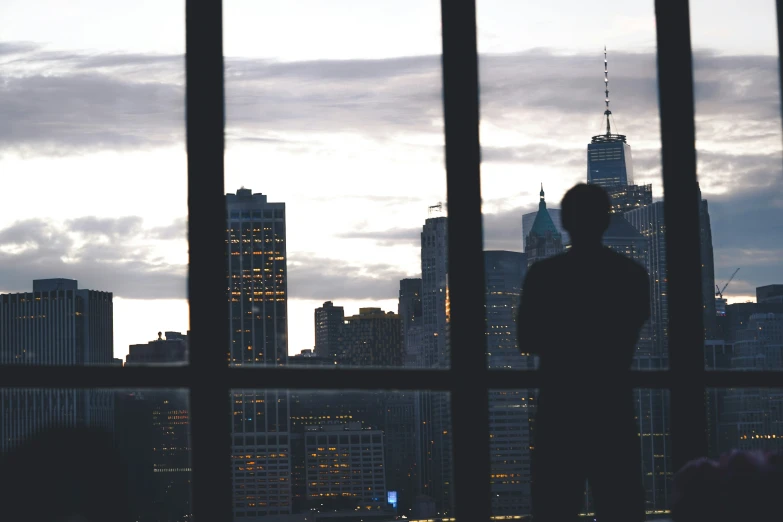 a city skyline through bars at twilight with a man looking at the skyline