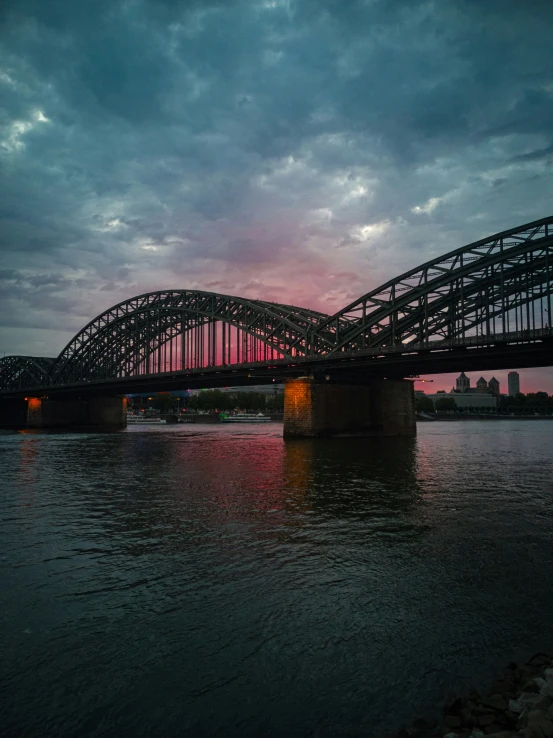 an iron bridge crosses the river into the sunset