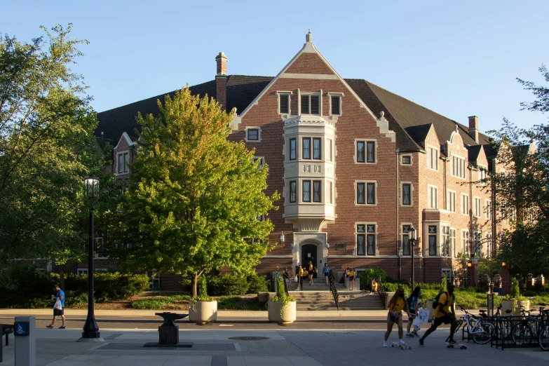 students walking on the cam sidewalk near a large, red brick building
