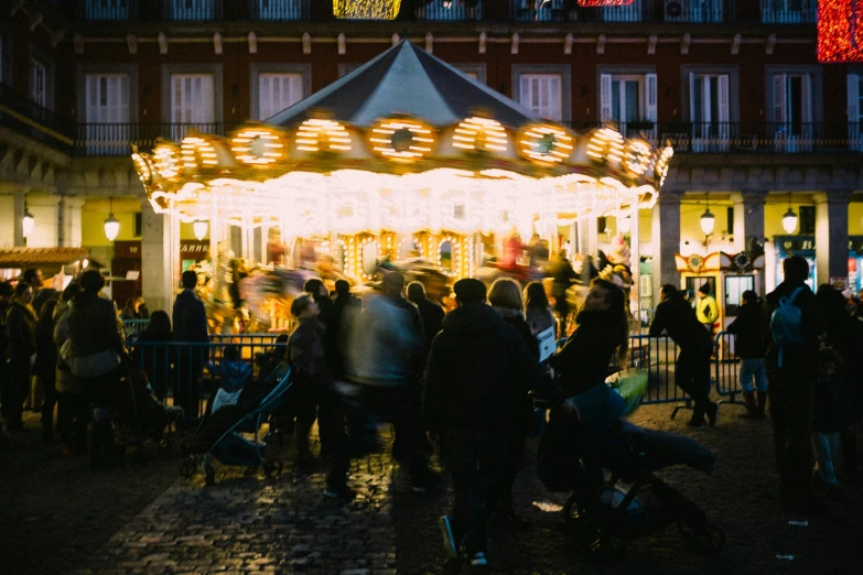 people are gathered around the carousel at night