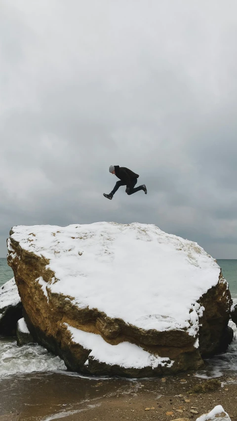 a man in black jacket jumping over rocks in snow