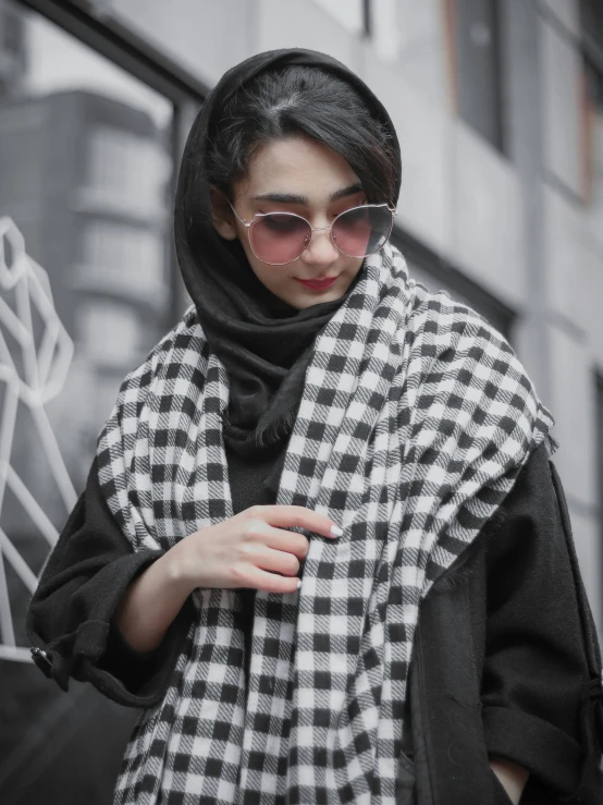 a woman in sunglasses is dressed in a plaid shawl