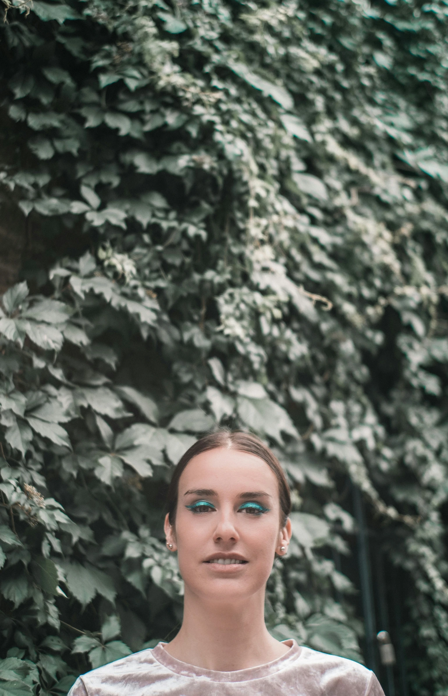 a woman posing for a picture in front of a large leafy wall