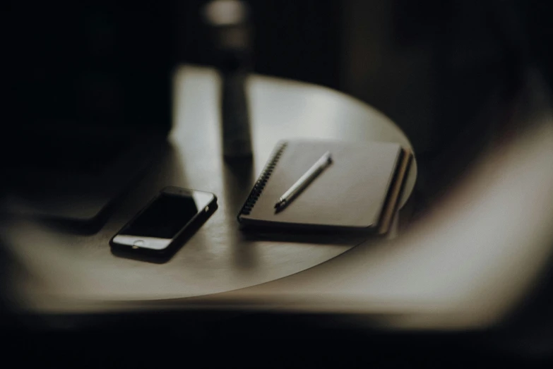 a desk that has a cell phone, pen and pen on it