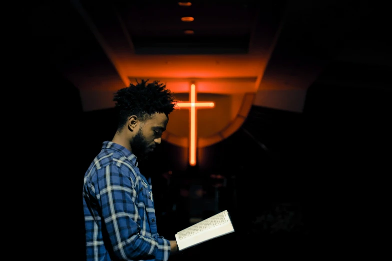 a man reading a book with a cross behind him