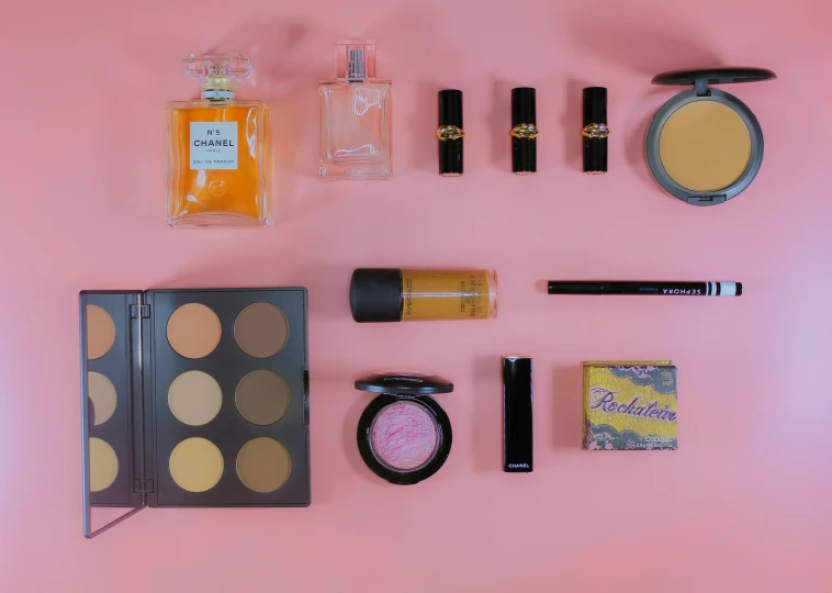 makeup and beauty products laid out neatly on a pink surface