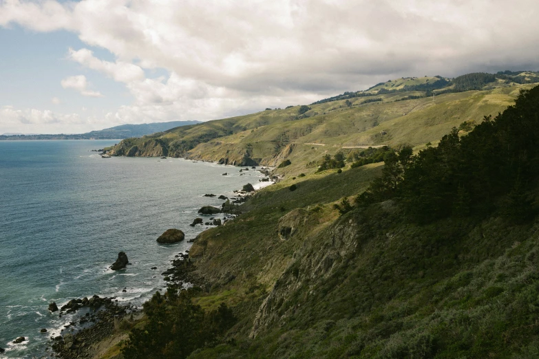 a hilly ocean shoreline next to mountains and the shore