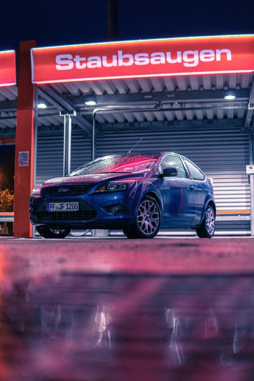 an blue car is parked on the curb in front of a stop sign at night